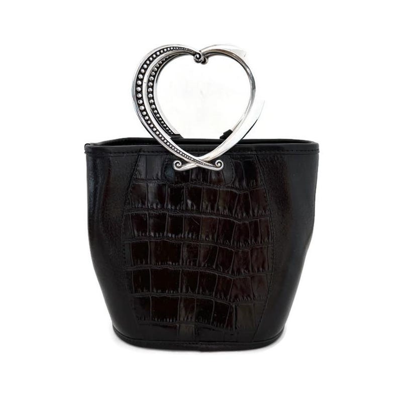 Pu&ograve; includere: Una borsa a mano in pelle nera con un manico a forma di cuore argentato. La borsa ha un motivo a stampa di coccodrillo.