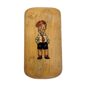 May include: A wooden brush with a cartoon illustration of a boy wearing a white shirt, red tie, and black shorts. The brush is rectangular and has a rounded top and bottom.