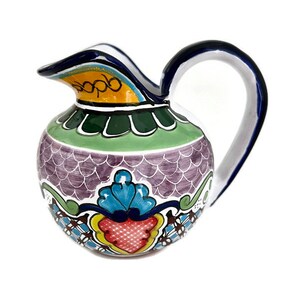 May include: A small, hand-painted ceramic pitcher with a purple, green, blue, yellow, and red floral design. The pitcher has a rounded body and a curved handle.