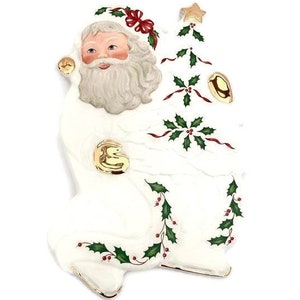 May include: A ceramic Santa Claus figurine in white with gold accents. Santa is holding a Christmas tree decorated with holly and red ribbons. The figurine has a jolly face and a long white beard, perfect for holiday decor.