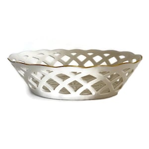 May include: White ceramic basket with a lattice design. The basket has a scalloped edge and a gold trim. This decorative basket is ideal for displaying fruit or other items.
