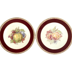 May include: Two vintage dessert plates with a red and gold rim. The plates feature a hand-painted design of fruit, including apples, plums, and berries.