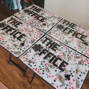 May include: Set of six folding tables with a playing card design. Each table features the text "THE OFFICE" in large black letters, with a poker chip graphic. The tables are supported by black metal legs.
