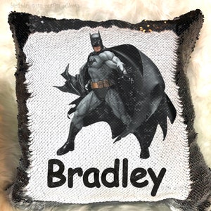 May include: A reversible sequin pillow featuring Batman in a dynamic pose. The pillow has a white background with a Batman graphic and the name "Bradley" in black. The border is black sequins.