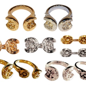 May include: Set of three horseshoe rings in gold, silver, and rose gold. Each ring features two horseshoe-shaped pieces connected by a band. The horseshoes are detailed with small raised dots.