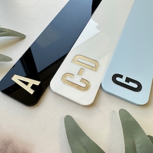 May include: Three rectangular signs with letters A, C-D, and G. The signs are black, white, and light blue. The letters are gold on the white sign and black on the blue sign.