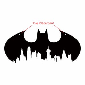 May include: A black Batman logo silhouette with a cityscape design at the bottom. The logo has two holes for hanging. The words "Hole Placement" are written in red, pointing to the holes.