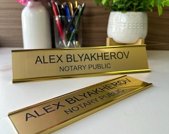 May include: Two gold desk nameplates with black lettering. The top plate reads "Alex Blyakheron Notary Public". The bottom plate reads "Alex Blyakheron Notary Public".
