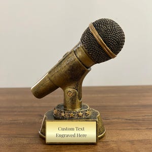 May include: Gold-tone microphone trophy with a black mesh microphone head and a base with a gold plaque that reads "Custom Text Engraved Here".