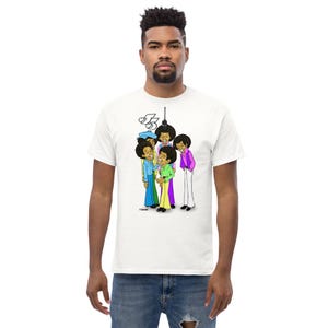 May include: White t-shirt featuring a cartoon illustration of a group of people in colorful outfits. The illustration includes the number "5" and a microphone. The figures are wearing blue, green, purple, and pink clothing.