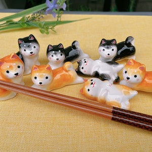 May include: A set of ceramic dog chopsticks rests on a yellow tablecloth. The chopsticks are in the shape of dogs, with some dogs lying down and others standing up. The chopsticks are painted in black, white, and orange.