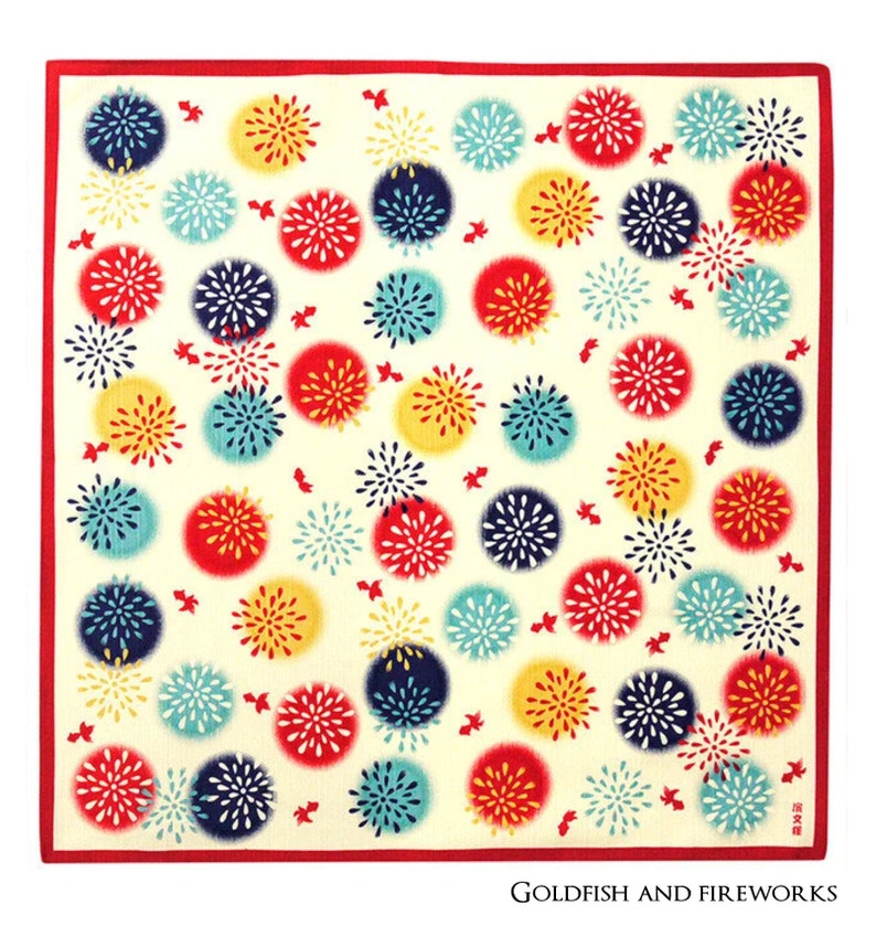 Op de afbeelding: Een wit vierkant van katoenen stof met een rode rand. De stof is bedrukt met een herhalend patroon van kleurrijke vuurwerk in rood, geel, blauw en groen. De tekst "Goldfish and Fireworks" is in zwart gedrukt aan de onderkant van de stof.