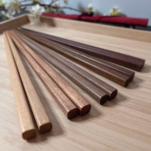 May include: A set of eight pairs of wooden chopsticks in various shades of brown, arranged in a fan shape on a wooden surface.
