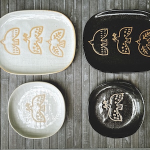 May include: Set of four ceramic plates with a white and black speckled glaze. Each plate features a stylised bird design in gold.