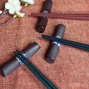 Peut inclure: Quatre paires de baguettes avec des supports en céramique décoratifs. Les supports sont bruns et présentent un motif floral bleu et blanc. Les baguettes sont brun foncé et noires.