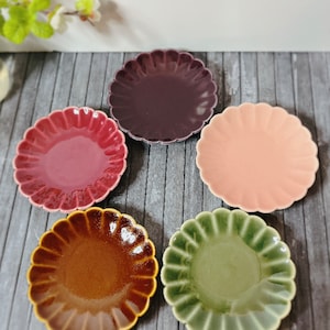 May include: Four small, decorative plates with scalloped edges. The plates are in shades of brown, green, pink, and purple.