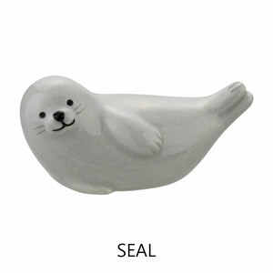 May include: A ceramic seal figurine in a reclining pose. The seal is a light gray color with a black nose, eyes, and whiskers. The word "SEAL" is printed in black below the figurine.