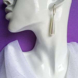 May include: A pair of white teardrop-shaped earrings with silver hooks.