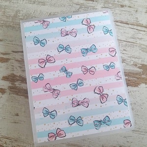 Puede incluir: Una carpeta de pl&aacute;stico transparente con un patr&oacute;n de lazos rosas y azules sobre un fondo blanco. Los lazos est&aacute;n dispersos por la carpeta y son de varios tama&ntilde;os. La carpeta tiene un borde blanco alrededor de los bordes.