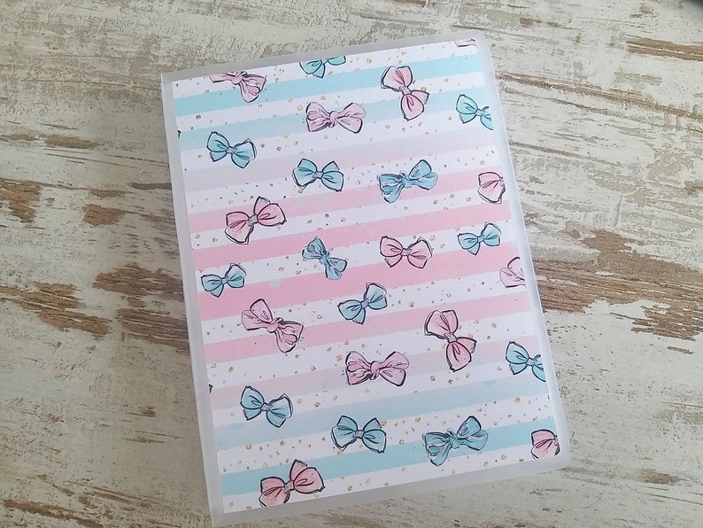 Puede incluir: Una carpeta de pl&aacute;stico transparente con un patr&oacute;n de lazos rosas y azules sobre un fondo blanco. Los lazos est&aacute;n dispersos por la carpeta y son de varios tama&ntilde;os. La carpeta tiene un borde blanco alrededor de los bordes.