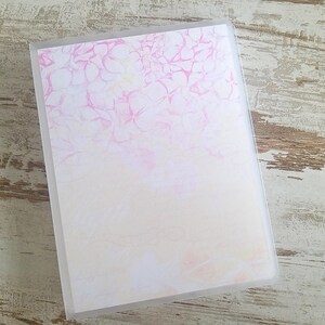 Puede incluir: Un archivador de pl&aacute;stico transparente con un dise&ntilde;o floral rosa y blanco en la parte delantera. El dise&ntilde;o es de estilo acuarela con un degradado de rosa a blanco.