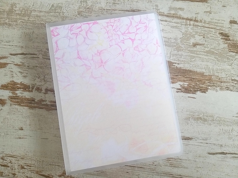 Puede incluir: Un archivador de pl&aacute;stico transparente con un dise&ntilde;o floral rosa y blanco en la parte delantera. El dise&ntilde;o es de estilo acuarela con un degradado de rosa a blanco.