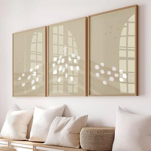 Könnte beinhalten: Drei gerahmte Kunstdrucke mit beigem Hintergrund und Fensterdesign. Die Drucke hängen über einer Bank mit weißen Kissen und einem geflochtenen Korb. Die Rahmen sind hellbraun.