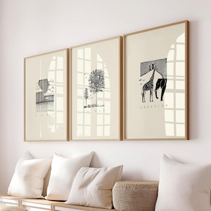 May include: Three framed art prints with minimalist black and white illustrations. The prints feature a landscape, a tree, and a giraffe with an elephant. The words "LOAD", "SALE", and "CREATION" are printed below the images. The frames are light brown.