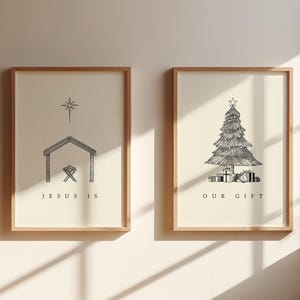 Op de afbeelding: Twee ingelijste kunstdrukken met een beige achtergrond. Eén toont een kerststal met de tekst "JESUS IS". De andere toont een kerstboom met cadeaus en de tekst "OUR GIFT". Beide zitten in houten frames.