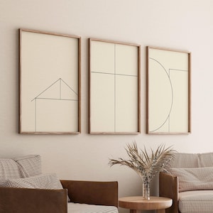 Könnte beinhalten: Drei gerahmte minimalistische Linienkunstdrucke mit beigefarbenem Hintergrund und schwarzen Linien. Die Drucke hängen an einer weißen Wand. Die Drucke zeigen geometrische Formen, darunter ein Haus, ein Kreuz und ein Halbkreis.
