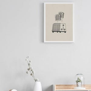 Puede incluir: Una ilustraci&oacute;n en blanco y negro de una tostadora con dos rebanadas de pan que salen disparadas. La ilustraci&oacute;n est&aacute; sobre un fondo beige y enmarcada con un marco blanco.