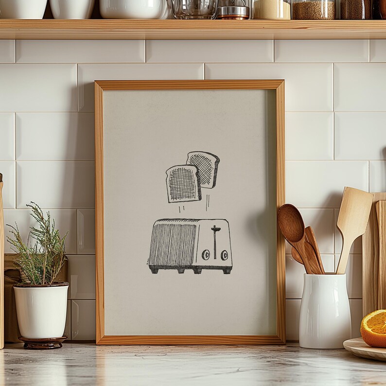 Puede incluir: Una ilustraci&oacute;n en blanco y negro de una tostadora con dos rebanadas de pan que saltan. La ilustraci&oacute;n est&aacute; enmarcada en un marco de madera claro y est&aacute; colgada en una pared de azulejos blancos.
