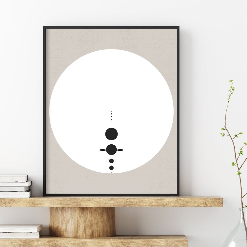 May include: A black and white minimalist print of a solar system with a white circle in the background and a beige frame.