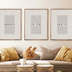 May include: Three framed prints with the text "SERMON ON THE MOUNT" in black text on a white background. The prints are hanging on a white wall above a beige couch with two throw pillows.