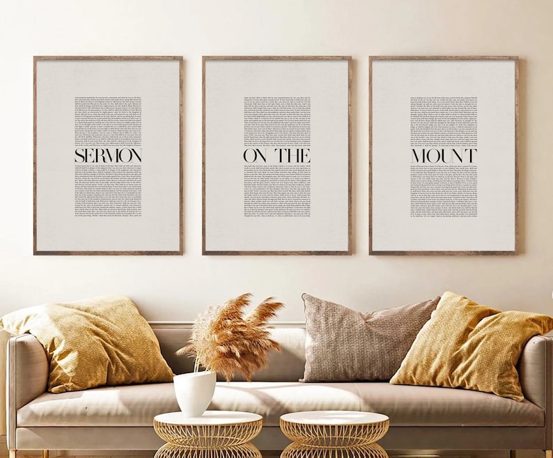 May include: Three framed prints with the text "SERMON ON THE MOUNT" in black text on a white background. The prints are hanging on a white wall above a beige couch with two throw pillows.