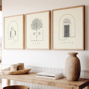 Puede incluir: Tres impresiones artísticas enmarcadas con dibujos lineales minimalistas. Las impresiones presentan las palabras "ASK", "SEEK" y "KNOCK". La obra de arte incluye ilustraciones de manos en oración, un árbol y una puerta. Los marcos son de color marrón claro y el fondo es crema.