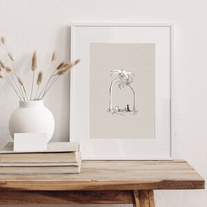 May include: A black and white line drawing of two people sitting under a palm tree. The drawing is framed in a white frame and is sitting on a wooden table.