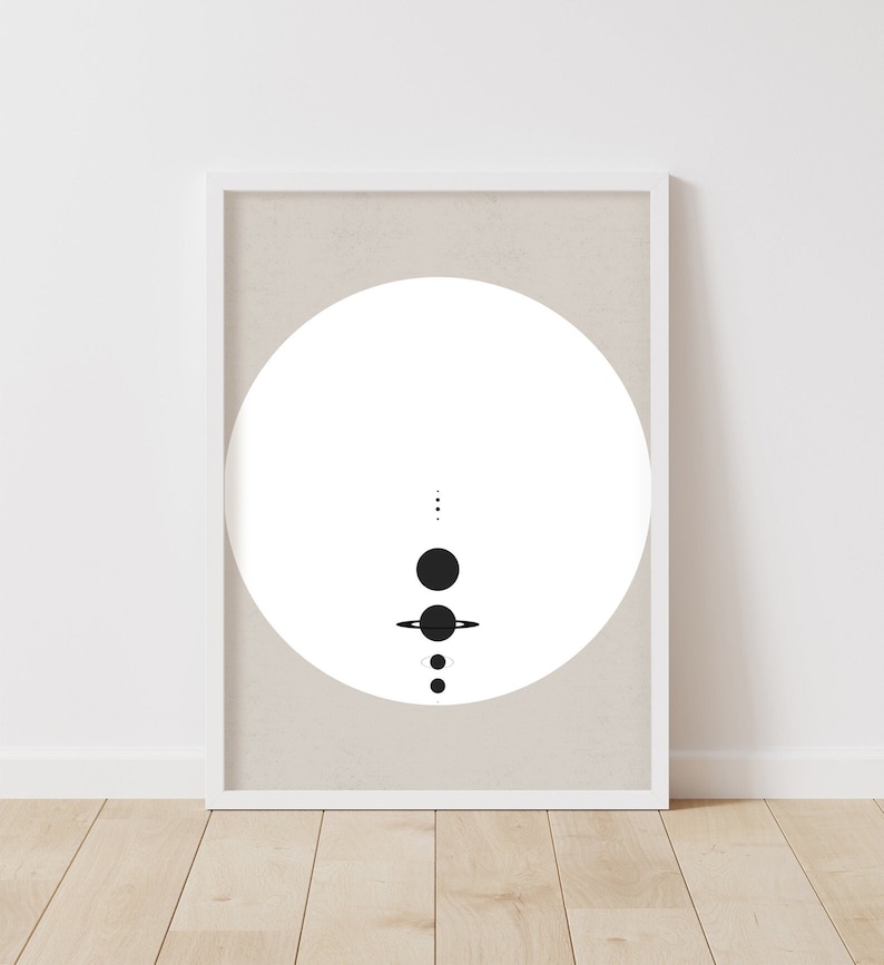 May include: A black and white minimalist print of a circle with a stylised solar system inside. The print is framed in a white frame and is hanging on a white wall.