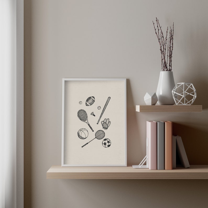 K&ouml;nnte beinhalten: Ein gerahmter Kunstdruck mit schwarz-wei&szlig;en Illustrationen von Sportger&auml;ten. Dargestellt sind ein Baseballschl&auml;ger, Tennisschl&auml;ger, ein Football, ein Basketball, ein Fu&szlig;ball und ein Baseballhandschuh. Der Druck befindet sich auf einem Holzregal.