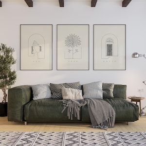 Puede incluir: Tres impresiones art&iacute;sticas enmarcadas con dibujos lineales minimalistas. Las impresiones presentan las palabras "ASK", "SEEK" y "KNOCK" debajo de im&aacute;genes de manos, un &aacute;rbol y una puerta. Un sof&aacute; verde con cojines y una manta se encuentra debajo.