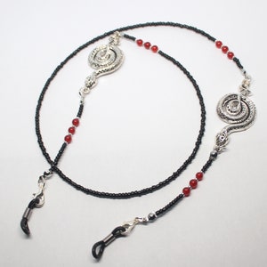 May include: Black beaded eyeglass chain with red beads and two silver snake charms.