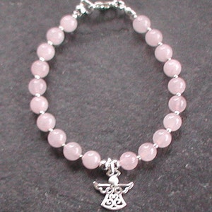 Może przedstawiać: Bransoletka z koralik&oacute;w z r&oacute;żowego kwarcu z zawieszką w kształcie srebrnego anioła.