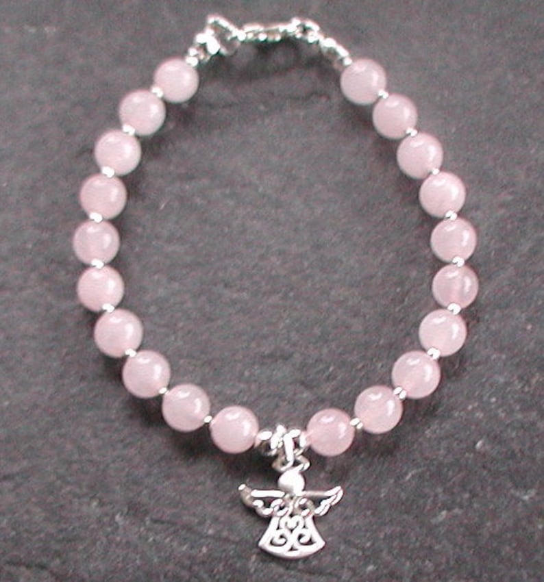 Może przedstawiać: Bransoletka z koralik&oacute;w z r&oacute;żowego kwarcu z zawieszką w kształcie srebrnego anioła.