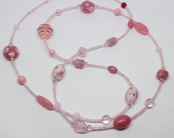 May include: A long pink necklace with various pink glass beads, including some with floral patterns. The necklace is made of two strands of beads.