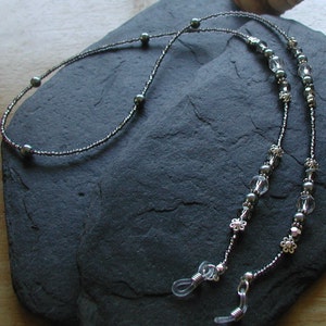 May include: A pair of black and silver beaded eyeglass chains with clear crystal beads and silver flower accents. The chains are attached to clear plastic eyeglass holders.