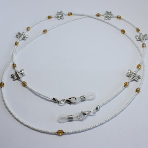 May include: White beaded glasses chain featuring silver bee charms and amber beads. The chain has clear rubber loops for glasses and silver clasps.