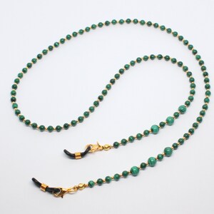 May include: A green and gold beaded eyeglass chain with gold clasps. The chain is made of small, round beads with a green malachite stone in the center of each bead.