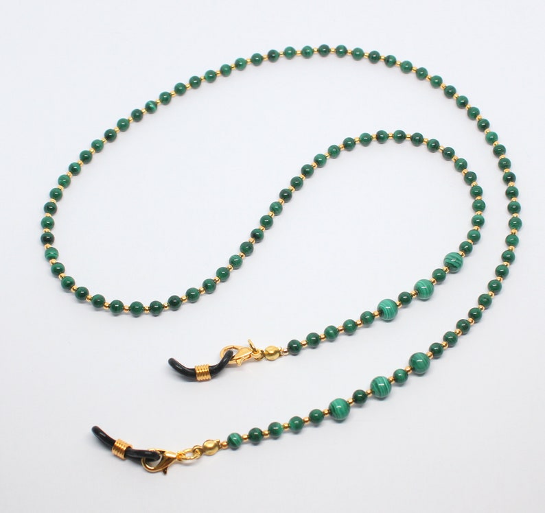 May include: A green and gold beaded eyeglass chain with gold clasps. The chain is made of small, round beads with a green malachite stone in the center of each bead.