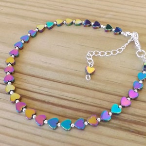 May include: A silver chain anklet with a rainbow iridescent heart charm. The anklet is made of small heart-shaped beads.