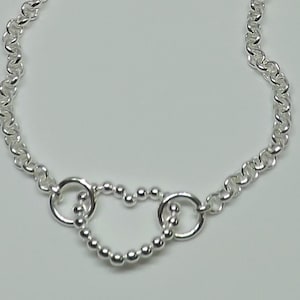 May include: A silver chain necklace with a heart-shaped pendant made of small silver beads. The heart is formed by two connected circles.